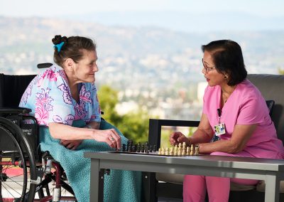 a staff member and a resident playing chess outdoors at the Valle Vista facility covered courtyard