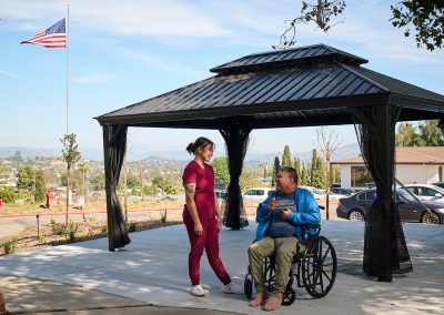 A caregivers with a resident in a wheelchair at the back courtyard of the Valle Vista facility