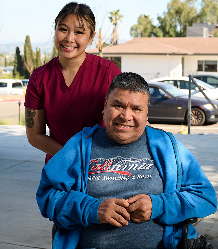 A caregivers with a resident in a wheelchair at the back courtyard of the Valle Vista facility