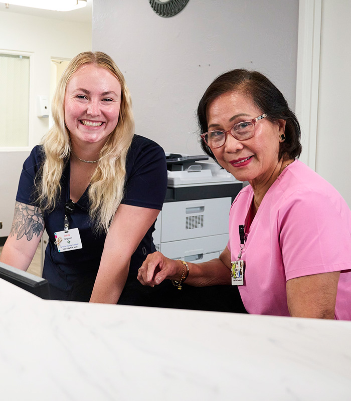 two nurses smiling behind the desk at the nurse station